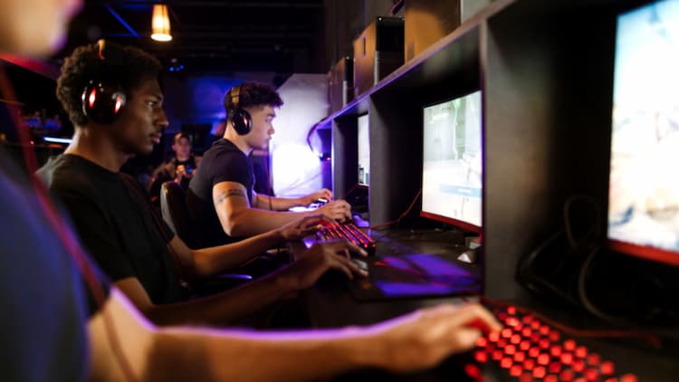 Row of people with headphones playing video games on PCs