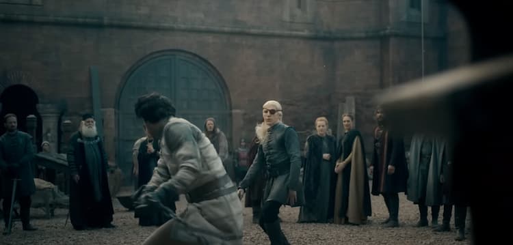 Two fighters sparring surrounded by armored onlookers in a castle yard. One has dark hair and another has light hair and an eye patch.