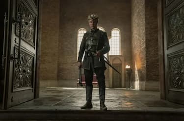 Daemon Targaryen stands alone at the open doors of the throne room wearing a crown made of bones.