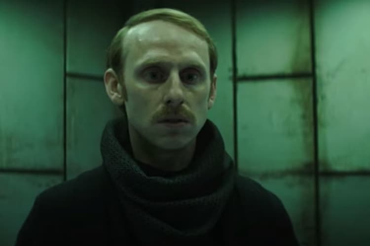 The ISB officer who is a spy looks towards the floor in realization.