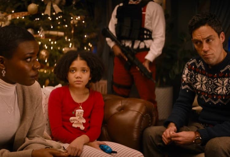 The Lightstone family sits in their Christmas-decorated living room while someone with body armor and a rifle stands behind them.