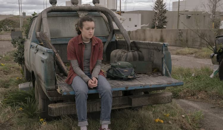 Ellie, lost in her thoughts, sits on a truck flatbed