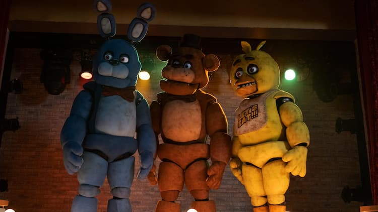 Bonnie, Freddy, and Chica are staring to the left. They're standing on the stage with a brick wall and multi-coloured lights behind them