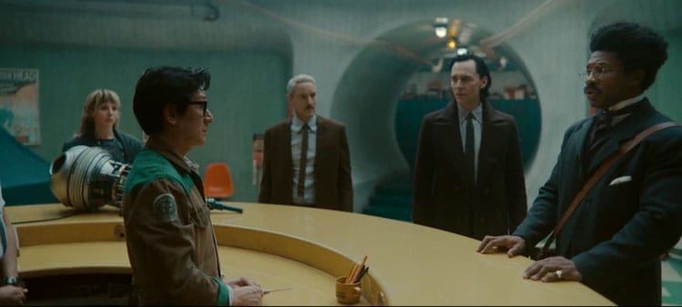 O. B. and Victor Timely are staring at each other in shock. They are both holding their books. Loki is talking to Mobius while Sylvie is looking bored to the left.