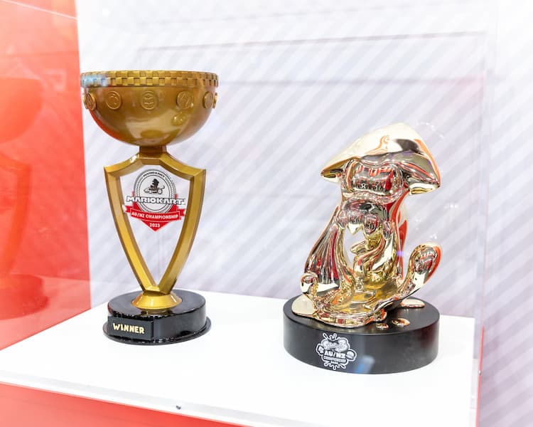 Two golden trophies are in a glass case. The one on the left is a typical trophy and is for Mario Kart 8 Deluxe. The one on the right is in the shape of a squid and is for Splatoon 3