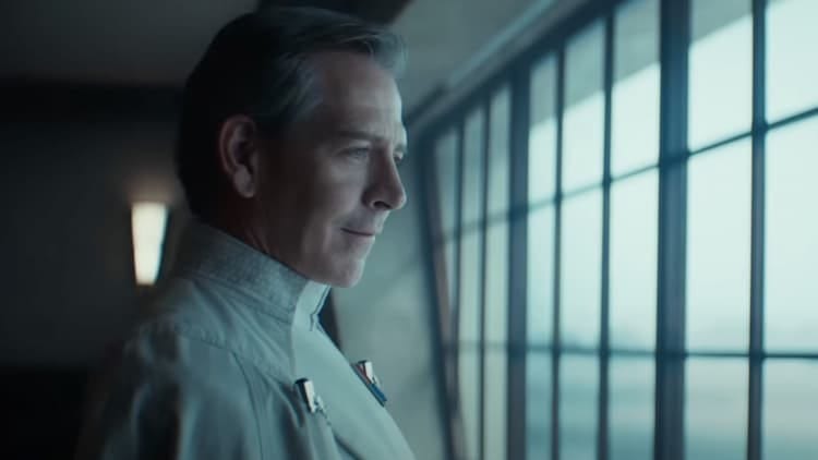Director Krennic is looking out a window. It's a cloudy day, and not much light is entering the room. He has a smile on his face.