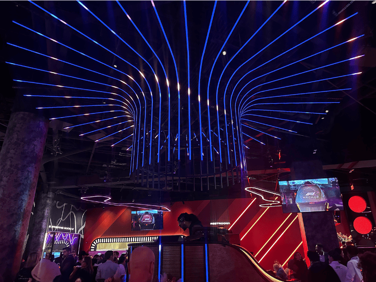 Dark lighting and neon blue light fixture at F1 Arcade. It's above a DJ booth with a live DJ.