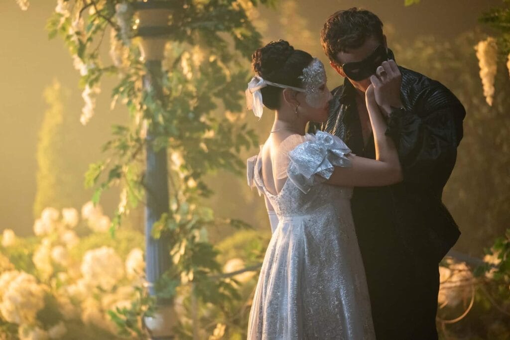 Benedict Bridgerton and Sophie Baek share an intimate moment at a masquerade ball in Bridgerton Season 4, both wearing elegant Regency-era attire and decorative masks under soft lighting.