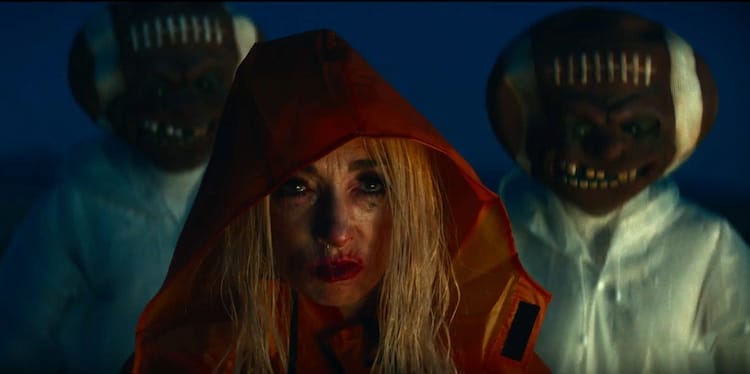 A woman with blonde hair in a red cloak and two men wearing scary-looking football headwear.