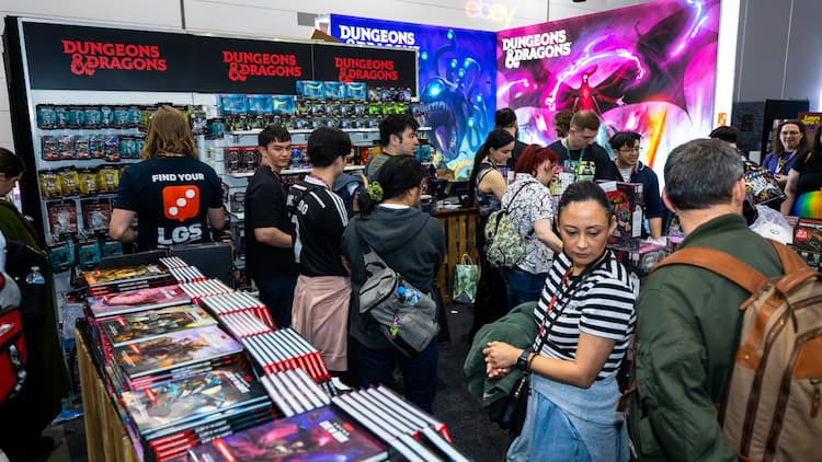 The Dungeons & Dragons store in the tabletop area at PAX Aus 2025. People are walking through the area, and some are buying products. Various pieces of merchandise are scattered throughout the booth.