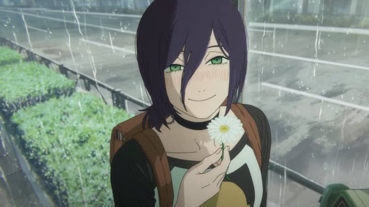 Reze is smiling while holding a white flower. She is blushing. It is raining outside. Plants and the road are in the background.
