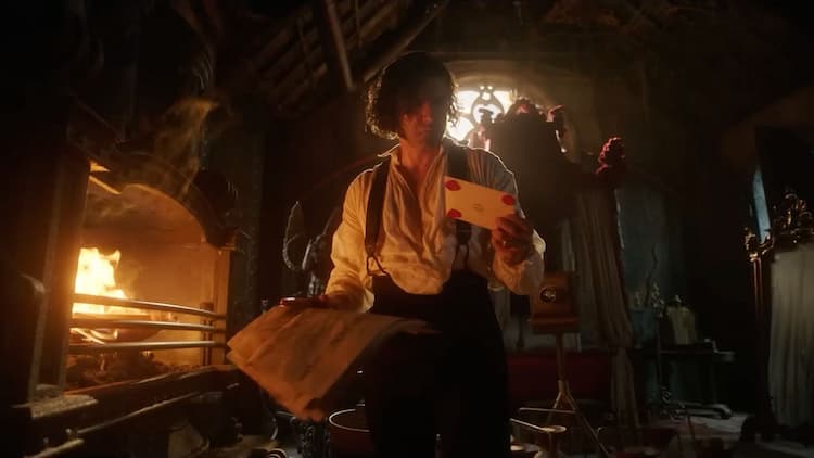 Victor Frankenstein is in a bedroom by himself. A fire is burning in the fireplace on the left. Victor is holding a letter in his left hand and a newspaper in his right. He is looking at the letter with indifference. Light is entering the room from the window at the back.