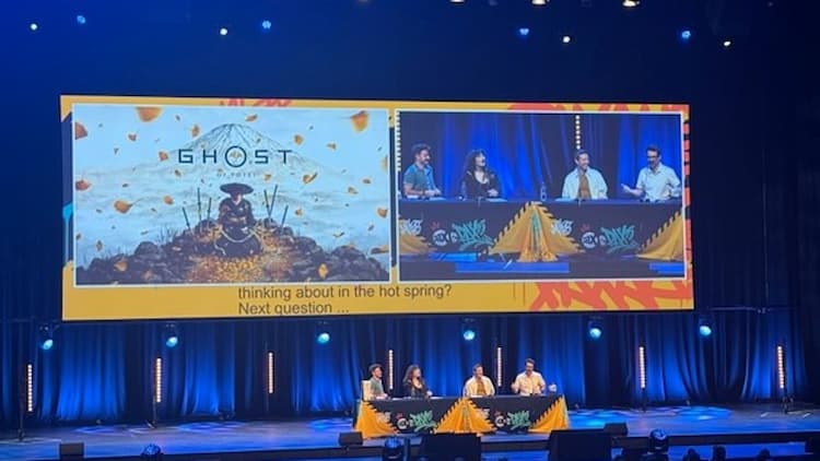 The Ghost of Yotei panel in the main theatre at PAX Aus 2025. The panellists are sitting at a table on the stage. The screen behind them has the key art for Ghost of Yotei on the left. A live feed of the panel is on the right.