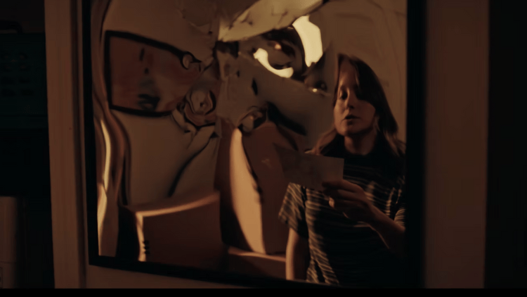 Isabella Roland in D(e)ad. She is holding a card and reading it out loud in front of a warped mirror.