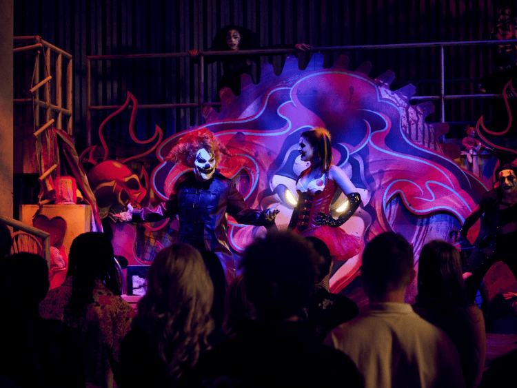 Jack the clown is on stage at Universal Horror Unleashed. He is a clown with red hair. There are other clowns on stage and several people in the crowd. 