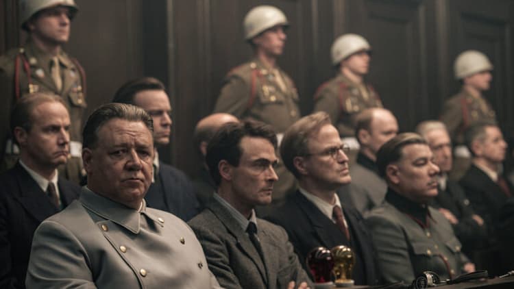 Goring and the rest of the Nazi prisoners are in a courtroom. Goring is looking to his left while the rest of the Nazis are looking in front of themselves. Military police are standing behind them.