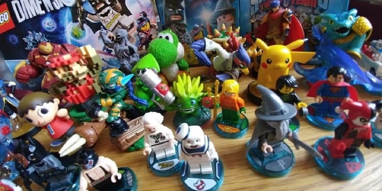 Various figures from a number of different toys-to-life games. The figures are on a wooden table with the game boxes behind them.