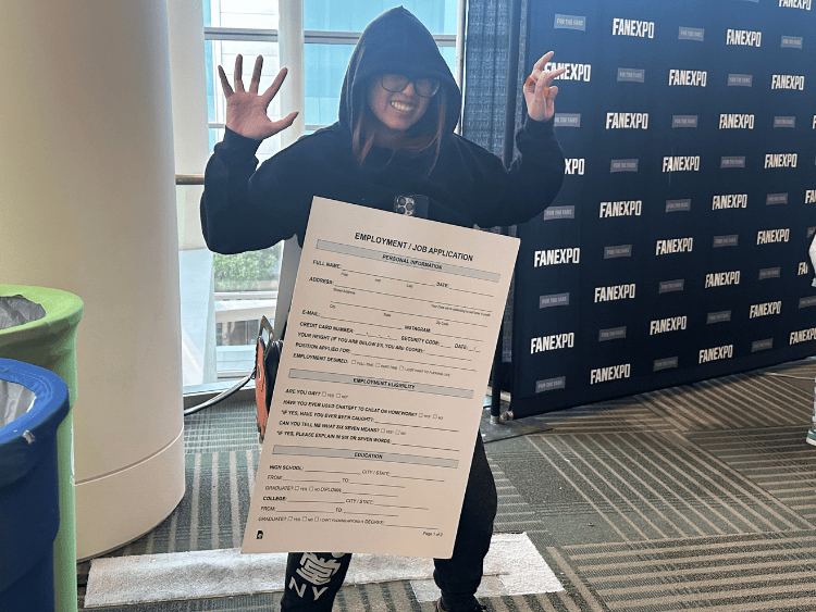 A cosplayer in all black with a massive sandwich board on the front that shows a blank job application