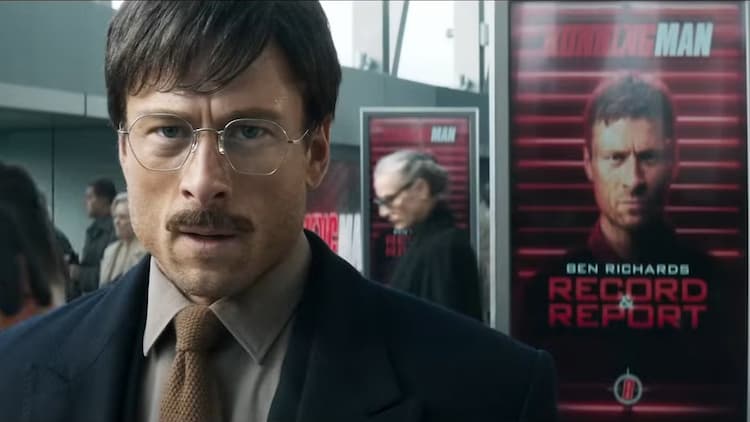 Ben Richards is in disguise. He is standing inside a building. Several ad boards behind him are displaying his face. People are walking by without paying much attention. Ben looks stressed.