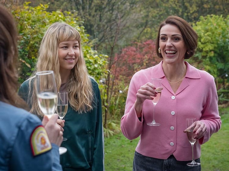 Evie, Izzy and Susanne are lifting wine classes and smiling. Susanne has a glass in both hands.