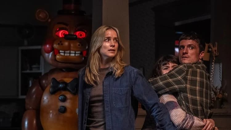 Vanessa, Mike, and Abby are huddled together in a house. Toy Freddy is approaching from the left with glowing red eyes. Vanessa, Mike, and Abby look scared.