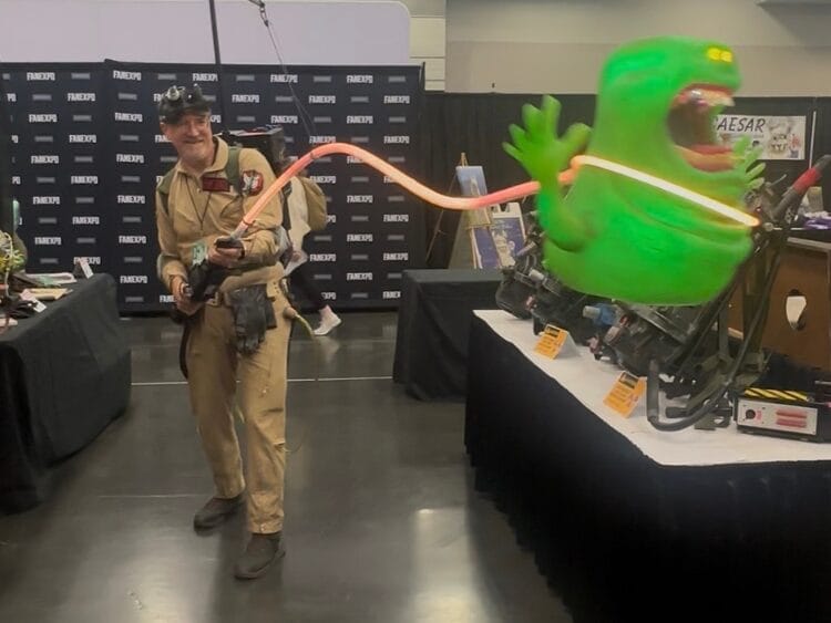 A man cosplaying as a ghostbuster is zapping a Slimer. It is very impressive.