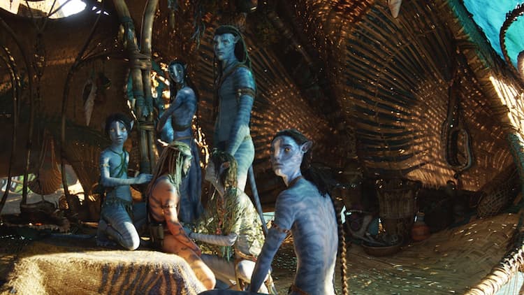 The Sully family and Spider are in a reef hut. Jake and Neytiri are standing in the back. Kiri is kneeling in front of Spider. Tuk is behind Spider. Lo'ak is at the edge of the hut. Neytiri, Jake, Tuk, and Lo'ak are looking in the same direction.