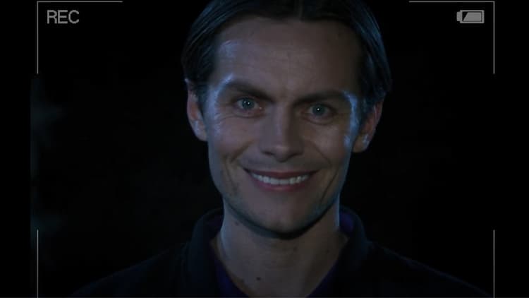 Michael Afton is smiling into a camera. He is standing in a parking lot at night. The camera display is around the border, with the recording symbol in the top-left corner and the battery in the top-right corner.